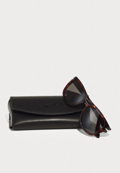 Occhiali da sole tartarugati con lenti scure appoggiati su un astuccio in pelle nera, con il marchio "Persol" inciso sulla parte anteriore.