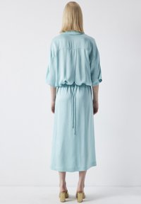 Un vestido azul claro, a la altura de la rodilla, con un corte relajado, que presenta mangas cortas, una cintura ajustable con lazo y una textura suave. Se muestra la vista posterior.