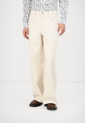 Beżowe spodnie typu wide-leg wykonane z bawełny o gładkiej fakturze. Posiadają kieszenie z przodu oraz zamek błyskawiczny z zapięciem na guzik.