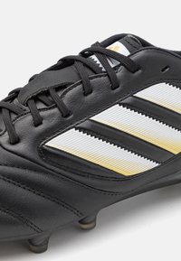 Black soccer cleat with leather material, featuring three white and gold striped accents and textured stitching. Includes black laces and studs.