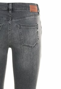 Jeans de color gris oscuro con un ajuste slim, diseño de cinco bolsillos y un parche trasero de cuero marrón con el logo de la marca. Textura de mezclilla suave, con un desvanecimiento mínimo.