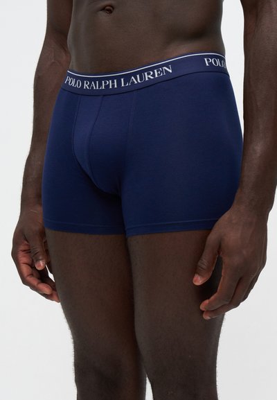 Άνδρας μοντέλο που φοράει μπλε σκούρο boxer Polo Ralph Lauren, εμφανιζόμενο από τη μέση έως το μέσο του μηρού σε απλό φόντο.
