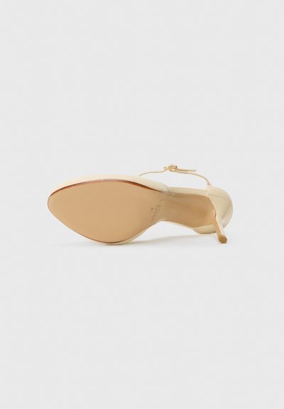 Chaussure à talon aiguille en cuir crème avec une ouverture à l'avant et une fine bride à la cheville. Talon stiletto et semelle lisse et courbée, accent en métal doré.