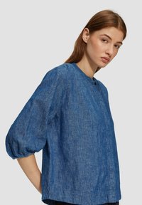 Blauwe chambray shirt met een ronde halslijn, belletjes mouwen en een knoopdetail aan de voorkant. Licht, gestructureerde stof met een casual pasvorm.