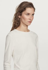 Langærmet creme top med rund halsudskæring, lavet af blødt stof, der har en glat tekstur og et simpelt design uden mønster eller detaljer.