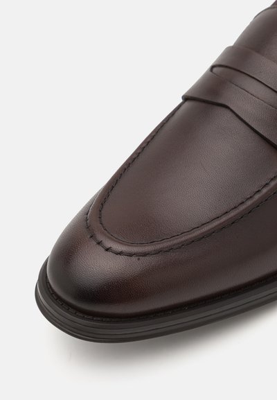 Pruun nahast loafers, millel on õmmeldud detailid, terav nina ja kummist tald. Sile tekstuur, minimalistlik disain ja nähtavaid riistu pole.