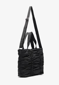 Schwarze Stofftasche mit geraffter Textur, ausgestattet mit zwei Griffen und einem verstellbaren Träger. Einfaches Design und glatte Oberfläche.