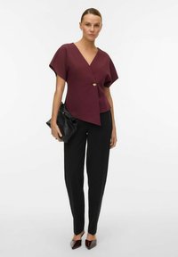 Vīna sarkans apņemšanas blūze ar īsām piedurknēm un zelta pogu priekšā, apvienota ar melniem piegriezuma biksēm un melnu clutcha somu.