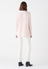 Maglione a maniche lunghe di un rosa chiaro, con una texture morbida, presenta un collo rotondo e polsini bianchi. Indossato con pantaloni bianchi e stivali neri con tacco.