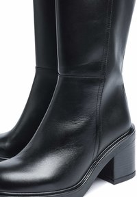 Botas de cuero negras hasta la rodilla con una textura suave, tacón grueso resistente y detalles de costura mínimos, que presentan un diseño elegante y moderno.