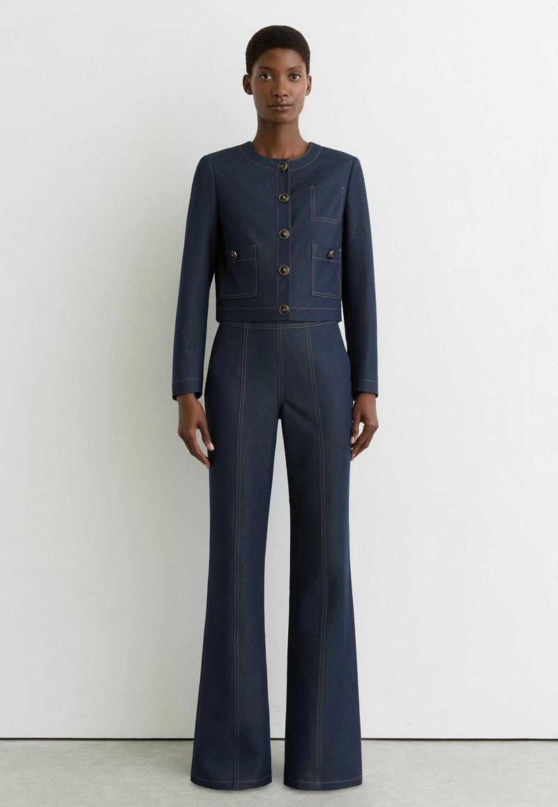 Ensemble veste en denim bleu foncé et pantalon évasé, avec boutons dorés, poches appliquées et détails de couture contrastants. Coupe ajustée.