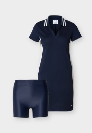 Tmavomodré šaty typu polo s bielymi bočnými panelmi a pruhovaným golierom v kombinácii s tmavomodrými priliehavými šortkami, obe s logom Puma.
