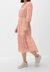 Kwiatowa sukienka midi w pomarańczowo-białym kolorze, z rękawami 3/4, marszczonym paskiem w talii i falbaniastej spódnicy, zestawiona z jasnymi trampkami.