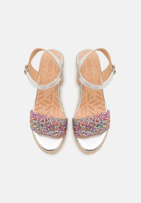 Sandales argentées avec une sangle tressée multicolore. Semelles en liège avec une texture florale. Sangle de cheville ajustable pour un bon maintien.