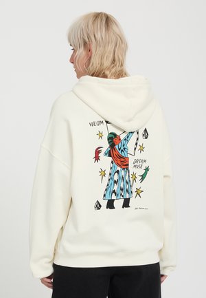 Persona rubia que lleva una sudadera blanca con capucha con una ilustración colorida de una figura con abrigo azul y bufanda roja en la parte trasera.