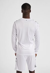 Hvid sportsjersey med lange ærmer og sorte detaljer på skuldrene, parret med hvide shorts. Lavet af glat, let materiale.
