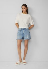 Witte short-sleeve shirt, lichtblauwe versleten denim shorts en stevige witte slidesandalen. Eenvoudig, ontspannen ontwerp met opgerolde shorts.