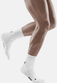White athletic socks with ribbed texture, mid-calf height, featuring black lettering and logo on the sides.