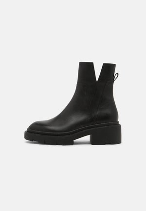 Bottine en cuir noir avec semelle épaisse et talon bloc, présentant une découpe en forme de V et un onglet à l'arrière.