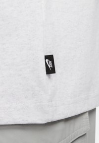 Vit bomullströja med en strukturerad yta, utrustad med en svart Nike-märkt broderad på sidan, som visar upp en minimalistisk design.