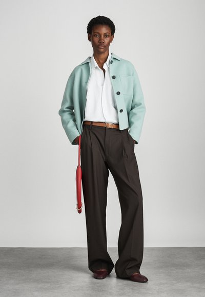 Μέντα πράσινο μάλλινο σακάκι, λευκό πουκάμισο, καφέ παντελόνι, κόκκινη τσάντα. Λείες υφές, χαλαρή εφαρμογή και μεγάλα κουμπιά στο σακάκι.