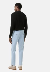 Lichtblauwe broek met achterzakken en een zwarte trui, gezien vanaf de achterkant. Beige schoenen met een textuurzool en zichtbare witte sokken.