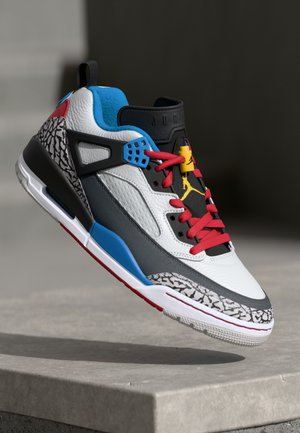 Tenis din piele albă cu accente gri și negre, șireturi roșii, călcâi albastru și logo galben. Prezintă modele texturate pe talpă.