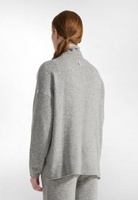 Grauer Strickpullover mit hohem Kragen, geripptem Saum und Seitenschlitzen. Verfügt über ein kleines pinkes Logo auf der Rückseite. Weicher Stoff, lockere Passform.