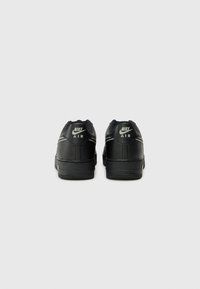 Sapatilhas Nike Air pretas expostas pela parte de trás, com um cabedal em pele lisa, colarinho almofadado e logotipo Nike branco com detalhes mínimos.