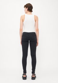 Črne skinny jeans z gladko teksturo, dvema zadnjima žepoma in srednje visokim pasom, v kombinaciji z belo majico brez rokavov in platformnimi čevlji.