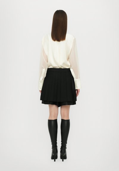 Blusa bianca con maniche traslucide, abbinata a una gonna plissettata nera e stivali neri con tacco al ginocchio. Design semplice ed elegante.