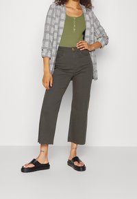 Šedý károvaný cardigan přes zelené žebrované tílko, doplněný olivovými zkrácenými kalhotami a černými skluznými sandály. Obsahuje knoflíky a boční rozparky.