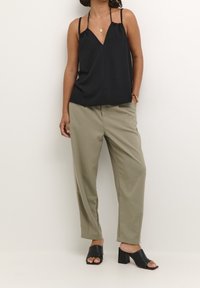 Zwarte camisole met dunne spaghettibandjes, V-hals ontwerp, gecombineerd met lichtkhaki geplooide broeken en zwarte open teen muiltjes met hakken.