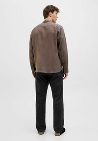 Brown, long-sleeved shirt made of lightweight fabric, featuring a relaxed fit, buttoned cuffs, and a collar, paired with black trousers.