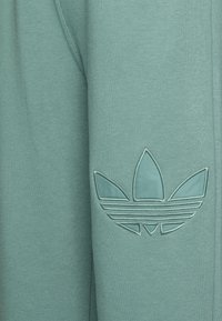 Gröna bomullssweatpants med en texturerad logotyp-applikation med blommönster och horisontella ränder på vänster lår.