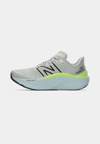 Sapatilha de corrida cinza da New Balance com logotipo preto, sola almofadada azul clara e detalhe em verde neon ao longo da entressola, vista de lado.