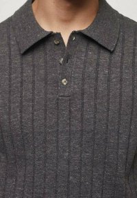 Harmaa neulottu polo-paita, jossa on ribbaustekstuuri, kaulus ja kolme nappia. Ominaisuuksiin kuuluu hillitty kiilto ja istuva siluetti.