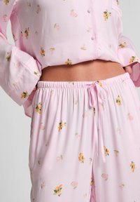 Roze pyjama set met een knoopsluiting op de lange mouwen en elastische taillebroek, versierd met bloemen- en fruitpatronen, gemaakt van zachte stof.