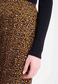 Leopardmönstrad kjol med brun botten, veckad design och svart ribbad långärmad tröja. En hand rör vid tyget nära midjan.