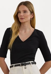 Zwarte V-hals top met korte mouwen, gemaakt van gladde stof. Gemaakt met een zwarte riem met een kleine metalen accent, gecombineerd met beige broeken.