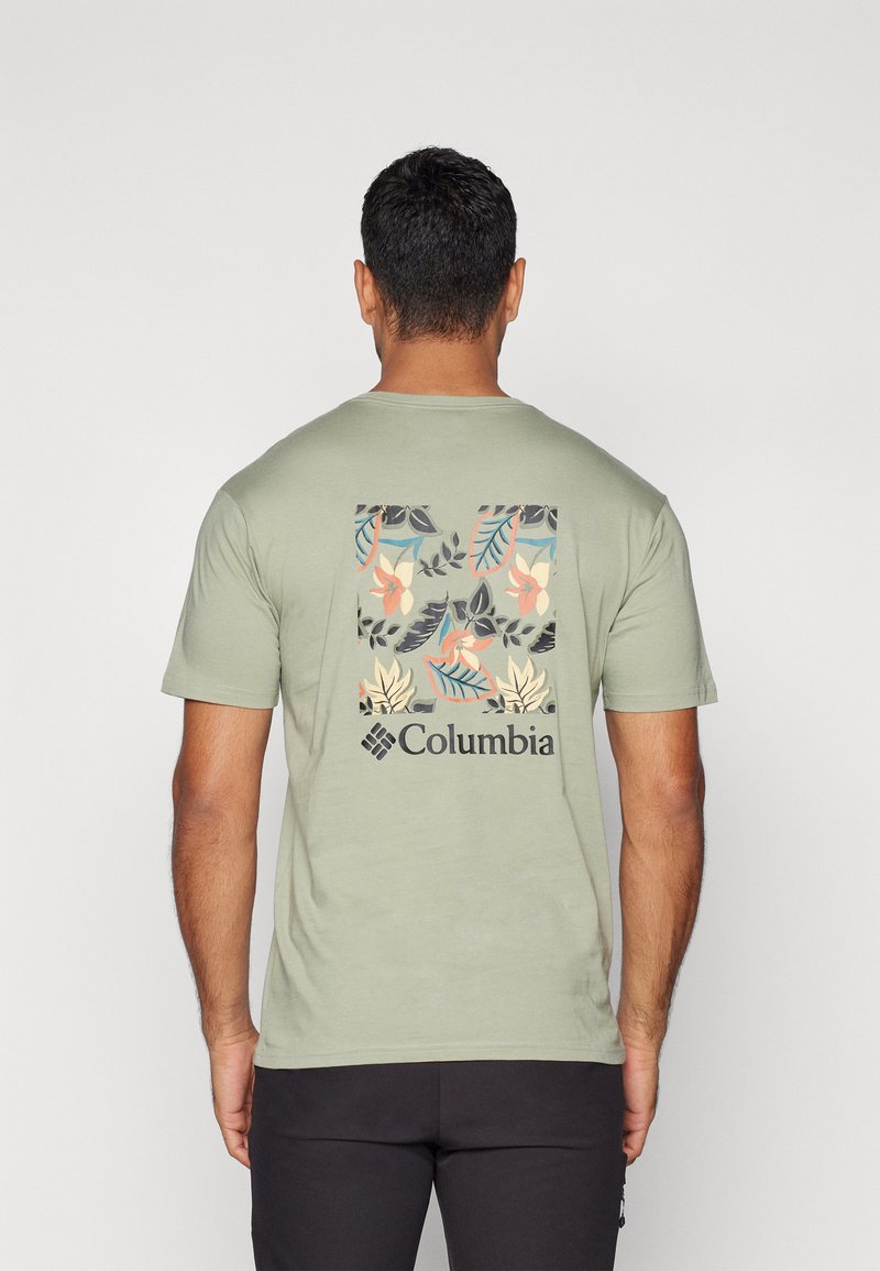 Oliven grønn kortermet t-skjorte med et blomstermotiv i myke farger på baksiden og en svart Columbia-logo under.