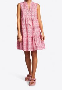 Vestido sin mangas rosa con cuello alto, patrón texturizado, falda en capas y detalle de lazo en el frente. Combinado con sandalias rosas con hebillas.