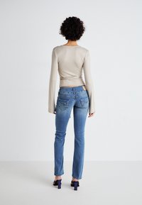 Haut nude à manches longues avec un design ajusté, associé à un jean en denim bleu clair avec des poches arrière et un léger effet délavé, porté avec des talons noirs.