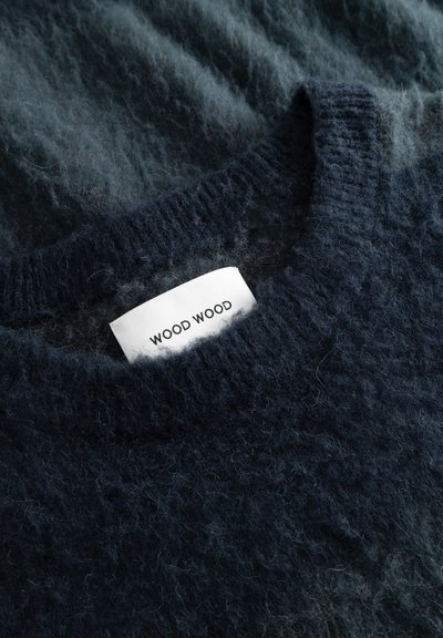 Ciemnoniebieski sweter o miękkiej, puszystej fakturze, z żeberkowym dekoltem i widoczną białą metką z napisem "WOOD WOOD" w kolorze czarnym.