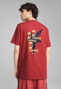 Camiseta de algodón roja con un diseño gr�áfico y texto amarillo y negro en la parte posterior, de mangas cortas y corte relajado.