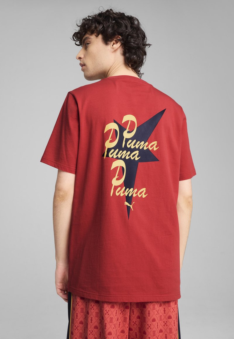 Camiseta de algodón roja con un diseño gráfico y texto amarillo y negro en la parte posterior, de mangas cortas y corte relajado.