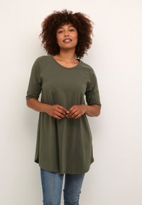 Tunique olive verte avec des manches courtes raglan, coupe décontractée, encolure ronde et tissu doux. Associée à un jeans bleu clair.