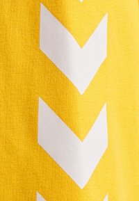 Tela amarilla con grandes patrones de chevron en blanco. La textura parece suave, con el patrón contrastando contra el fondo sólido.