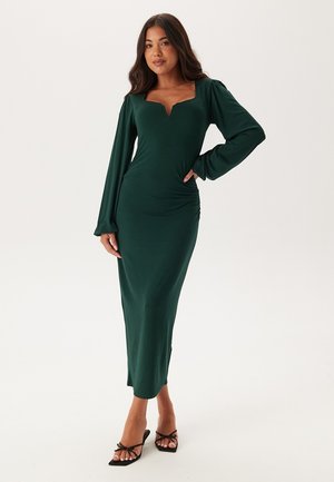 Robe verte à manches longues avec encolure carrée et détails froncés. Fabriquée en tissu lisse, au design ajusté et à coupe longueur cheville.