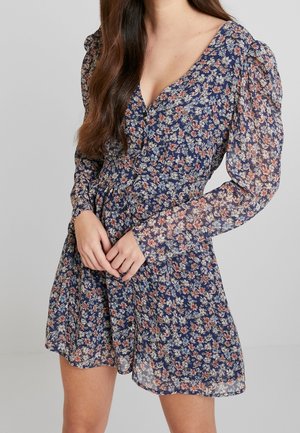 Floral-patterned dress in navy with a V-neck, long puff sleeves, cinched waist, and a flowing, lightweight fabric.